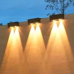 four lights are shining on the side of a wall with trees in the back ground