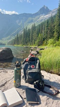 an open book, backpack and water bottle sitting on the edge of a cliff overlooking a mountain lake