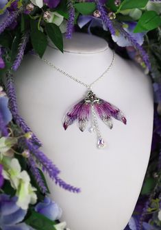 a white vase with purple flowers surrounding it and a necklace hanging from the neckline