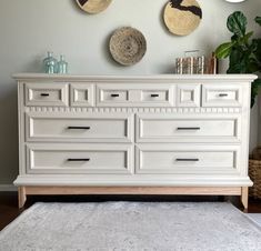 a white dresser sitting next to a wall with three baskets on it's top