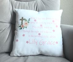 a white pillow with pink flowers and a cross on it sitting on a gray couch