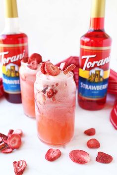 two glasses filled with ice cream and strawberries next to bottles of torani syrup