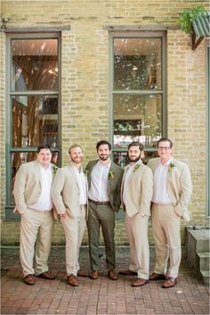 a group of men standing next to each other in front of a brick building with windows