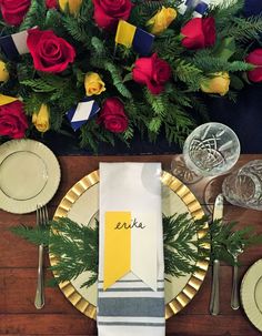 a place setting with plates, silverware and napkins on a wooden table surrounded by flowers