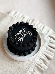 a black birthday cake sitting on top of a white plate with the words happy birthday written on it