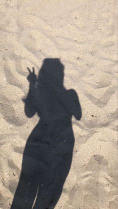 a shadow of a person holding a cell phone up to their ear in the sand