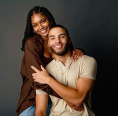 a man and woman hugging each other in front of a dark background with their arms around one another