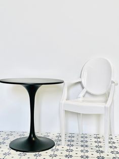 a white chair sitting next to a black table on top of a tiled floor in front of a white wall