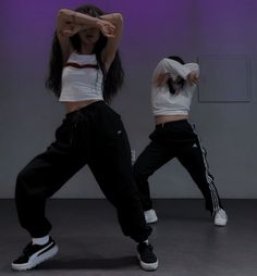 two women in white shirts and black pants are doing dance moves with their hands behind their head