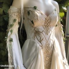 a white wedding dress with green leaves on the shoulders and sleeves, is displayed in front of a window