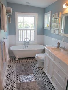 a white bath tub sitting under a window next to a toilet and sink in a bathroom