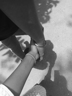 two people holding hands while standing next to each other on a skateboard in black and white