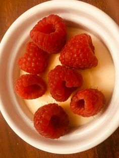 some raspberries are in a white bowl on a table