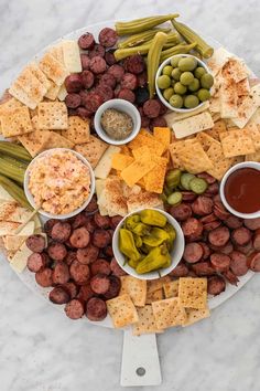 a platter filled with cheese, crackers, olives, and pickles