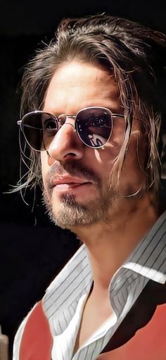 a man with long hair and sunglasses looks off to the side