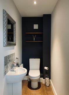 a white toilet sitting next to a sink in a bathroom under a mirror on top of a wooden floor