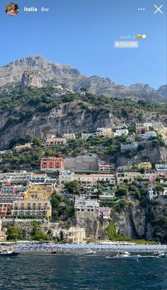 an image of a city on the side of a mountain with boats in front of it