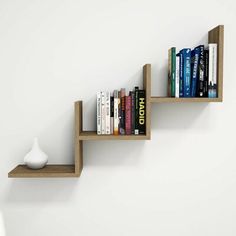 two wooden shelves with books on them against a white wall, one shelf has a vase and the other is empty