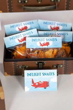 an open suitcase filled with snacks on top of a white table next to a sign that says in flight snacks