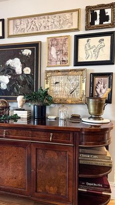 a room filled with lots of framed pictures on the wall above a wooden cabinet and sideboard