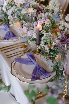 the table is set with purple and white flowers, gold rimmed plates, and silverware