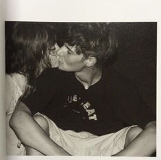 two people kissing each other while sitting on a bed in front of a black and white photo