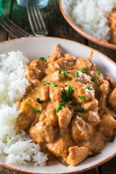 two plates filled with rice and meat covered in gravy on top of a wooden table