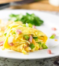 a white plate topped with an omelet covered in ham and vegetables next to chips