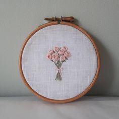 a close up of a embroidery on a wooden hoop with pink flowers in the center