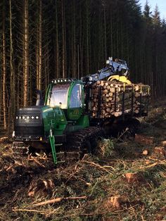 a green tractor is driving through the woods with logs on it's flatbed