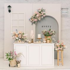 a table with flowers and cakes on it in front of a white wall that says avery