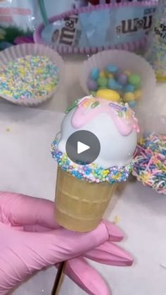 an ice cream cone with sprinkles and candy on it is being held by a glove