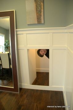 a man peeking out from behind a wall in a room with wood floors and white walls