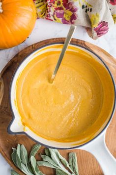 a wooden bowl filled with yellow sauce on top of a table next to pumpkins