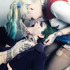 two women with green hair and piercings kissing on each other's cheek while wearing fishnet stockings