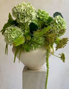 a white vase filled with green flowers on top of a cement block in front of a wall