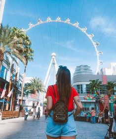 a woman walking down the street in front of a ferris wheel with her back to the camera