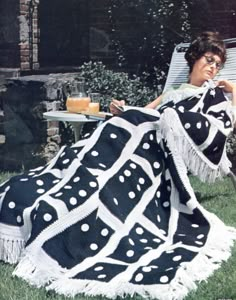 a woman sitting in a lawn chair under a black and white blanket with polka dots