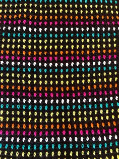 a multicolored crochet pattern on black fabric with white, yellow, pink, and blue dots