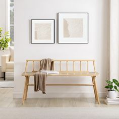 a wooden bench with two pictures on the wall above it in front of a window