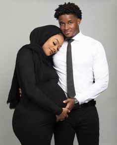 a man and woman hugging each other in front of a gray background with one wearing a white shirt and black tie