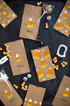 paper bags with candy corn on them sitting on a black surface next to halloween candies