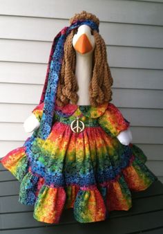 a stuffed duck wearing a colorful dress with peace sign on it's head and scarf around its neck