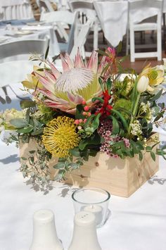 a wooden box filled with lots of flowers on top of a white cloth covered table