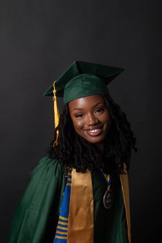 a woman wearing a green graduation gown and smiling at the camera with long curly hair