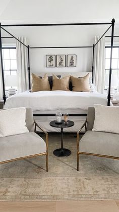 a bedroom with four poster bed, two chairs and a coffee table in front of it