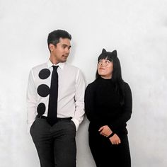 a man and woman standing next to each other in front of a white wall with black polka dots on it