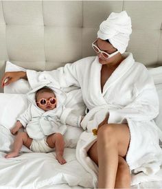 a woman in a bathrobe holding a baby while sitting on top of a bed