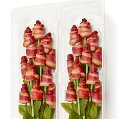 bacon wrapped asparagus are arranged in two plastic trays on a white surface