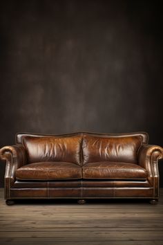 a brown leather couch sitting on top of a wooden floor next to a black wall